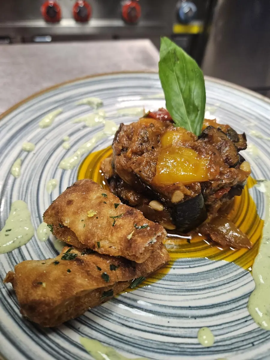 Specialità siciliana impiattata con verdure e basilico